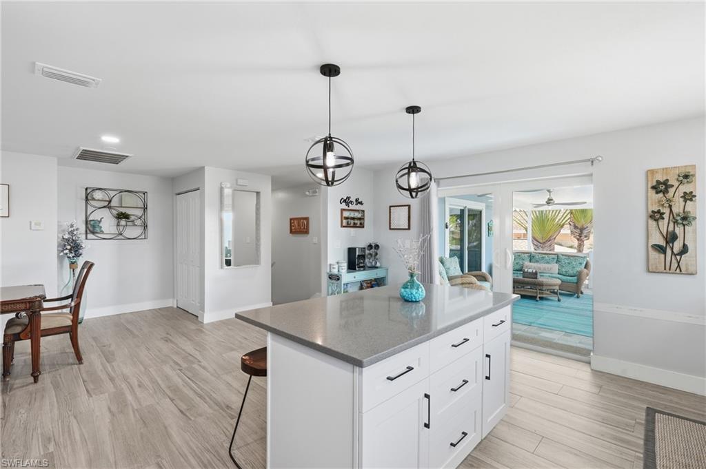 Kitchen island featuring a light-colored countertop, white cabinetry with dark hardware, and two pendant light fixtures - Virtually Edited Image