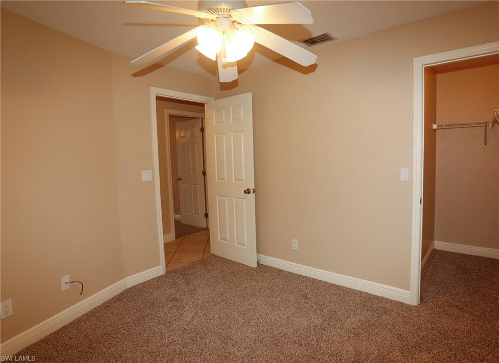 Carpeted room featuring a ceiling fan with integrated lighting, neutral wall paint, and white trim