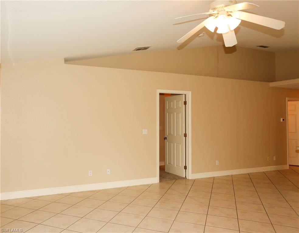 Spacious room featuring vaulted ceilings, a ceiling fan with integrated lighting, ceramic tile flooring, and neutral wall tones