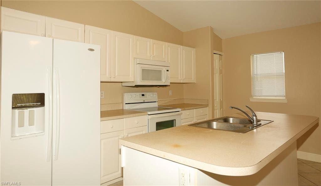 Kitchen featuring white cabinetry, light-toned countertops, a double basin sink with a chrome faucet, a white side-by-side refrigerator, and a white electric range with an overhead microwave