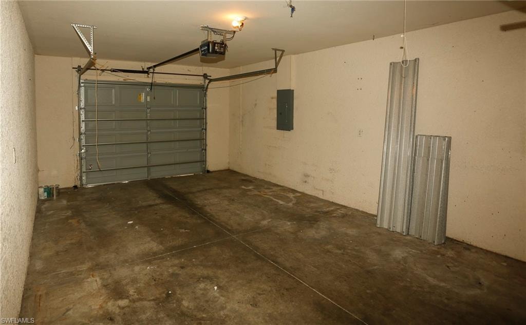 Concrete floor garage with an overhead garage door, automatic opener, and a wall-mounted electrical panel
