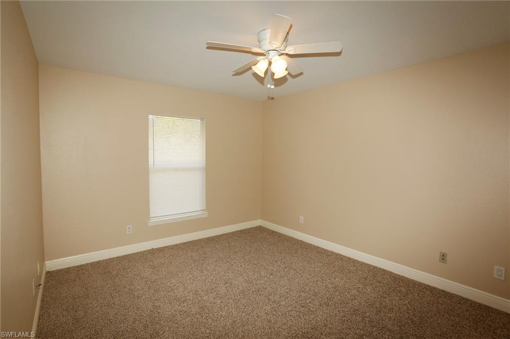 Interior room featuring neutral wall paint, a window with a roller shade, brown carpet flooring, white baseboards, and a ceiling fan with integrated lighting
