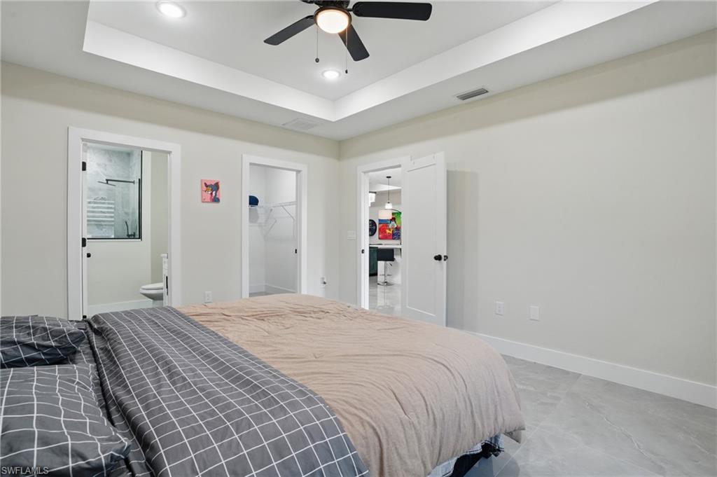 Bedroom featuring recessed lighting, a tray ceiling, baseboards, a walk in closet, and ensuite bathroom