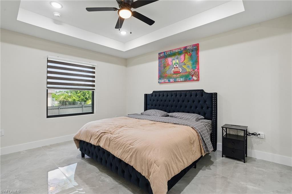 Bedroom featuring a tray ceiling, baseboards, recessed lighting, light marble finish floors, and ceiling fan
