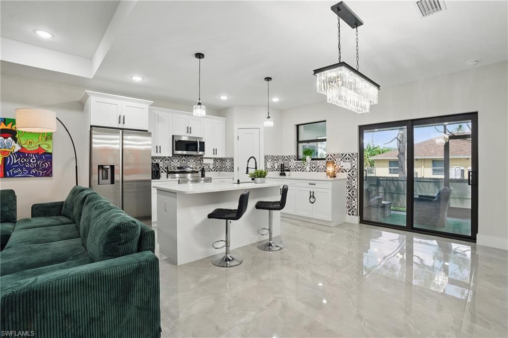Kitchen featuring stainless steel appliances, decorative backsplash, open floor plan, light countertops, and white cabinets