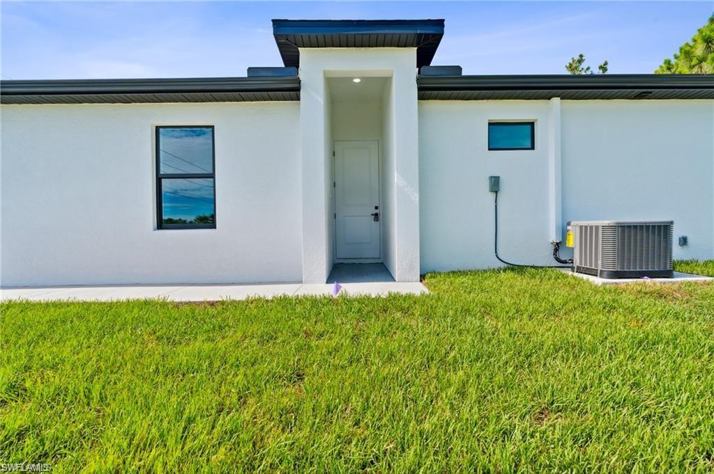 Rear view of property featuring central AC unit, stucco siding, and a yard