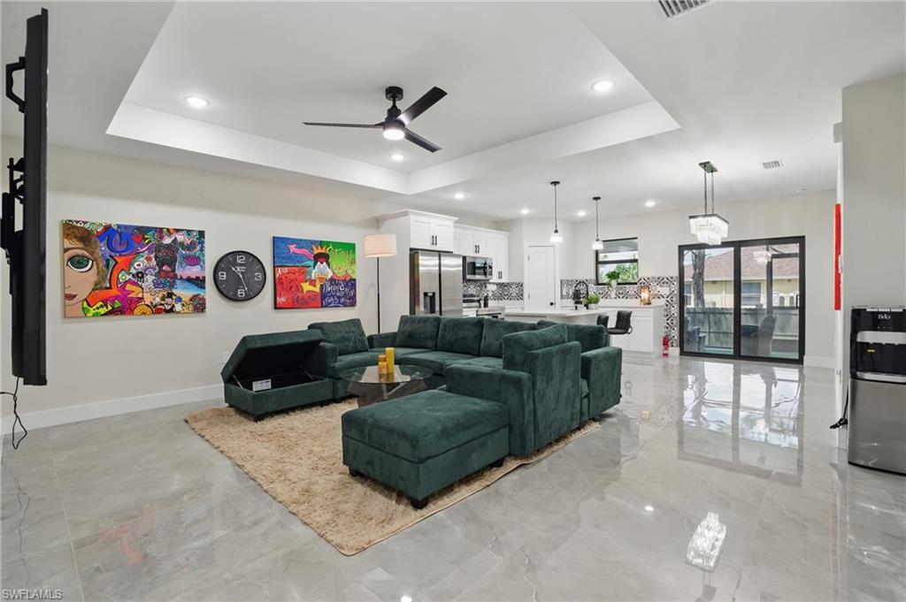 Living room with ceiling fan, light marble finish floors, a tray ceiling, recessed lighting, and baseboards
