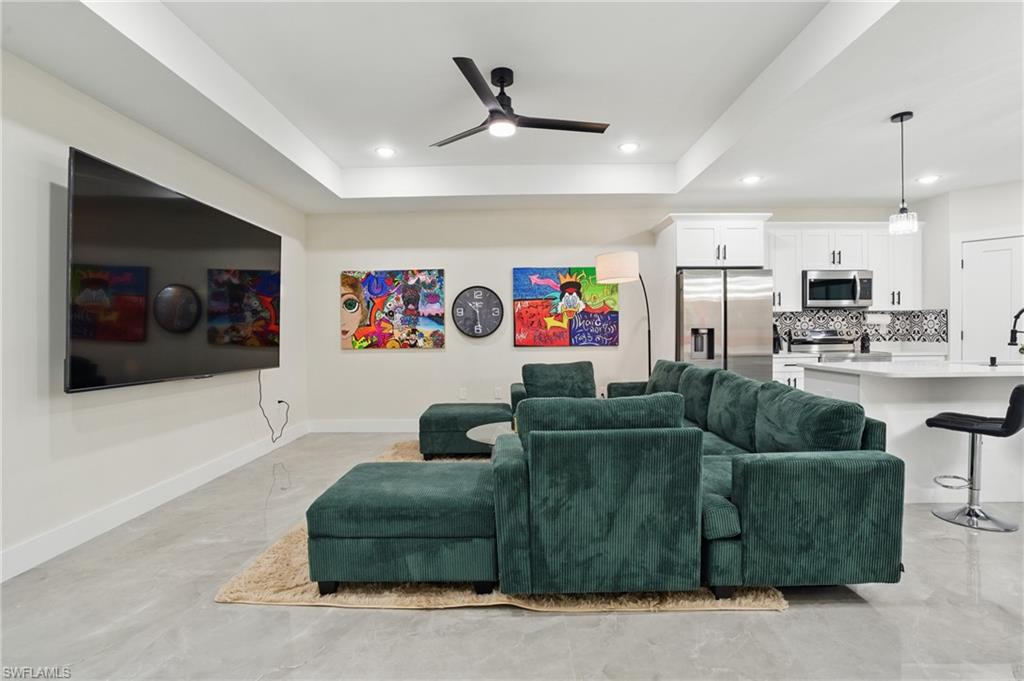 Living area with ceiling fan, a tray ceiling, baseboards, and recessed lighting