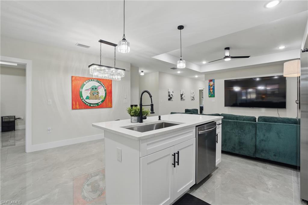 Kitchen featuring a sink, dishwasher, open floor plan, pendant lighting, and white cabinetry