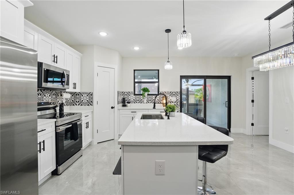 Kitchen with appliances with stainless steel finishes, a sink, decorative backsplash, light marble finish floors, and a kitchen island