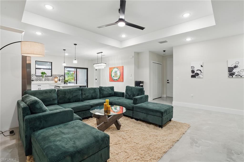 Living area featuring a ceiling fan, recessed lighting, a tray ceiling, and baseboards