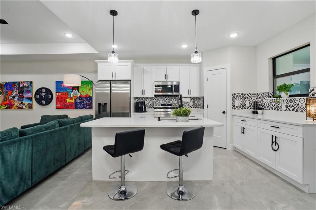 Kitchen featuring stainless steel appliances, tasteful backsplash, light countertops, white cabinetry, and a breakfast bar