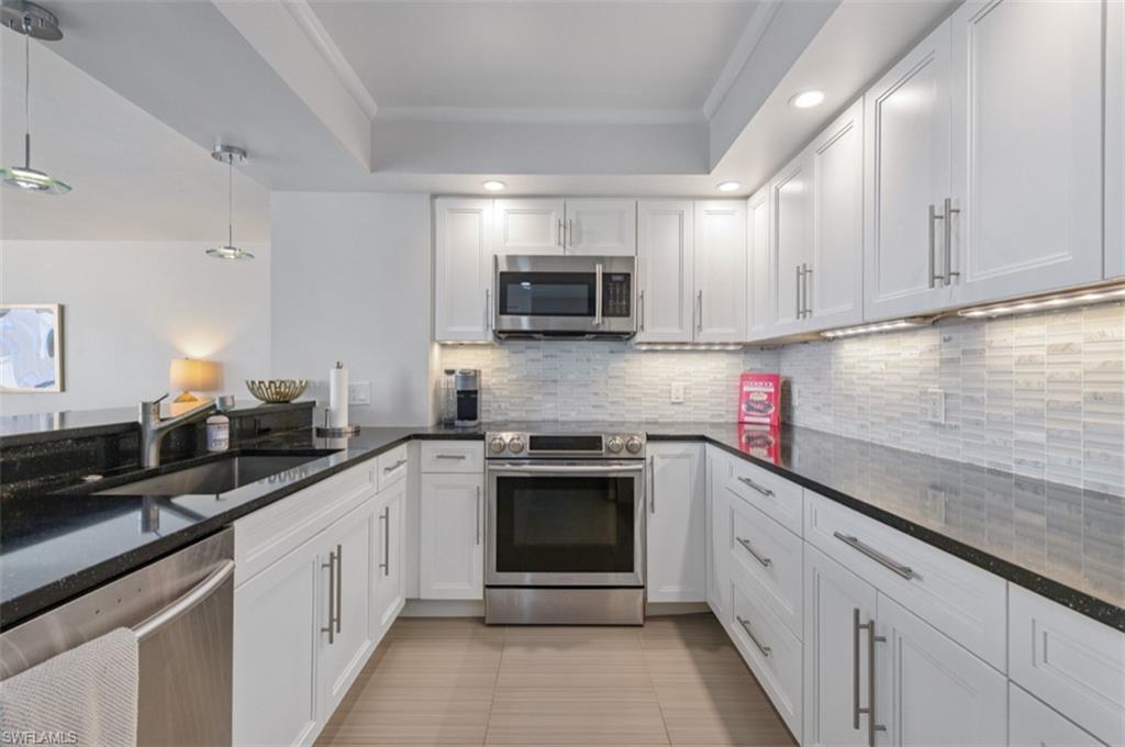 Kitchen featuring appliances with stainless steel finishes, decorative backsplash and white cabinets