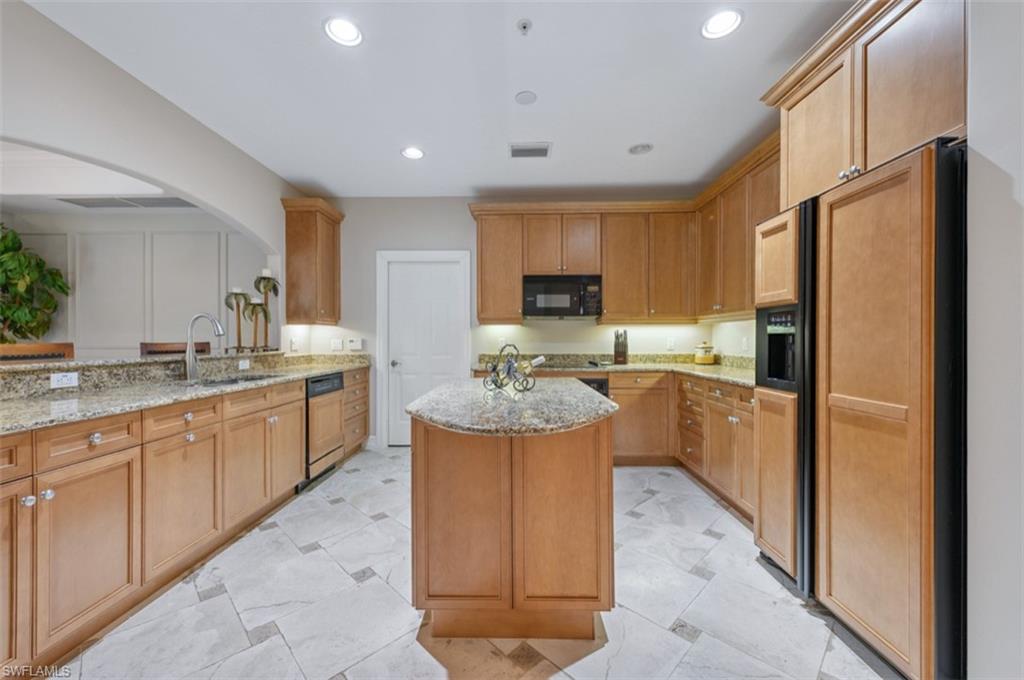 Kitchen with paneled fridge with ice dispenser, a kitchen island, light and stone countertops