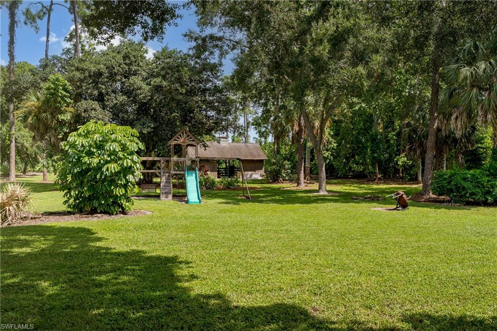 Expansive green lawn surrounded by mature trees, featuring a natural wood playset with a slide