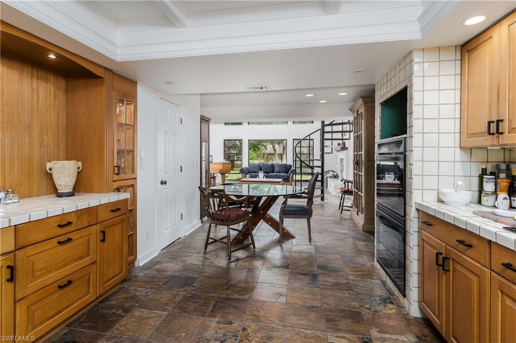 Kitchen area with light wood-finish cabinetry, tile countertops, and integrated double ovens