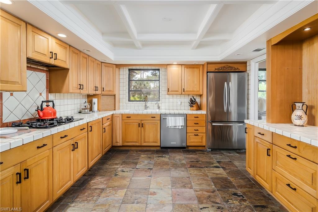 Functional kitchen featuring extensive wood cabinetry, stone tile flooring, white tile countertops, and a full suite of stainless steel appliances