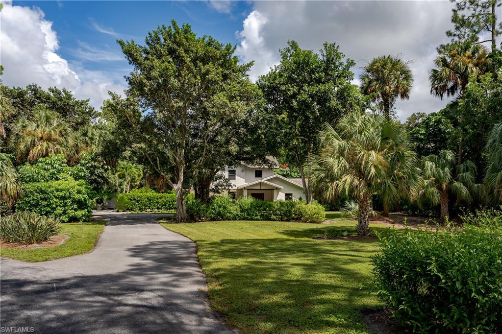 Lush tropical landscaping surrounds this residence, featuring a private driveway, mature palm trees, diverse greenery, and a manicured lawn