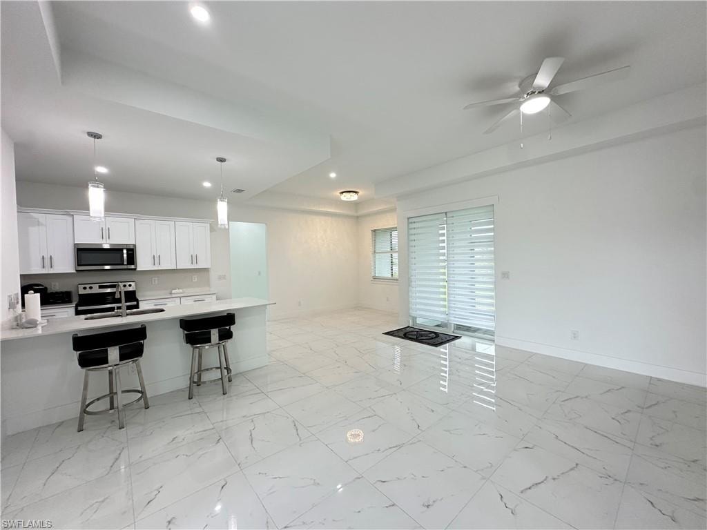 Open-concept living space featuring high ceilings, large format tile flooring, a contemporary kitchen with white cabinetry and stainless steel appliances, a kitchen island with pendant lighting, and sliding glass doors