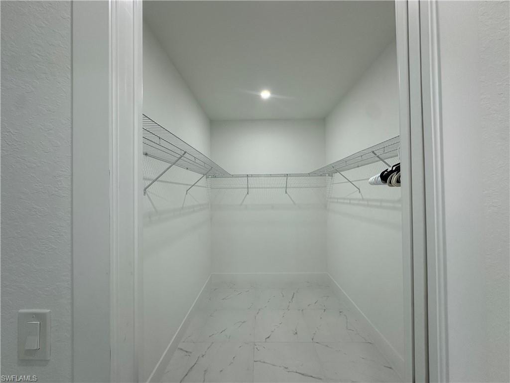 Spacious walk-in closet featuring white wire shelving, a recessed ceiling light, and marble-look floor tiling