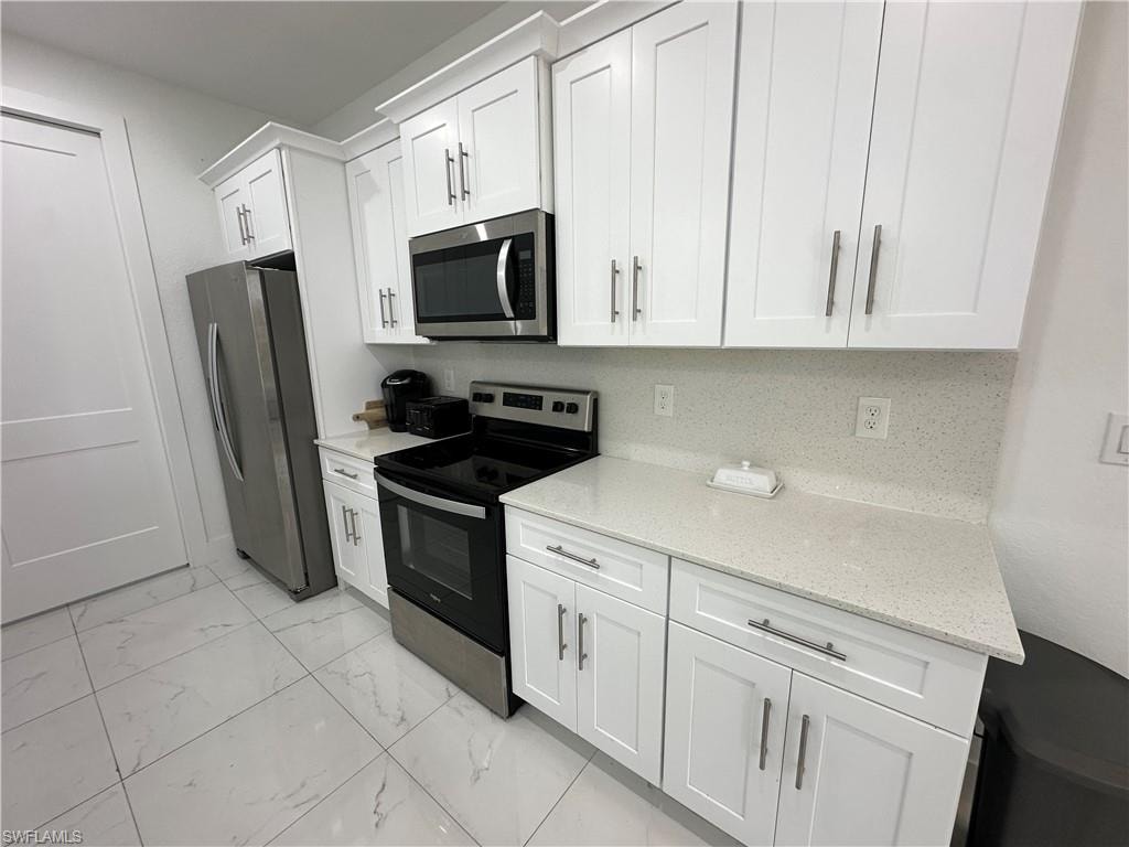 White shaker-style cabinetry with crown molding, stainless steel appliances, speckled solid surface countertops, and a coordinating backsplash