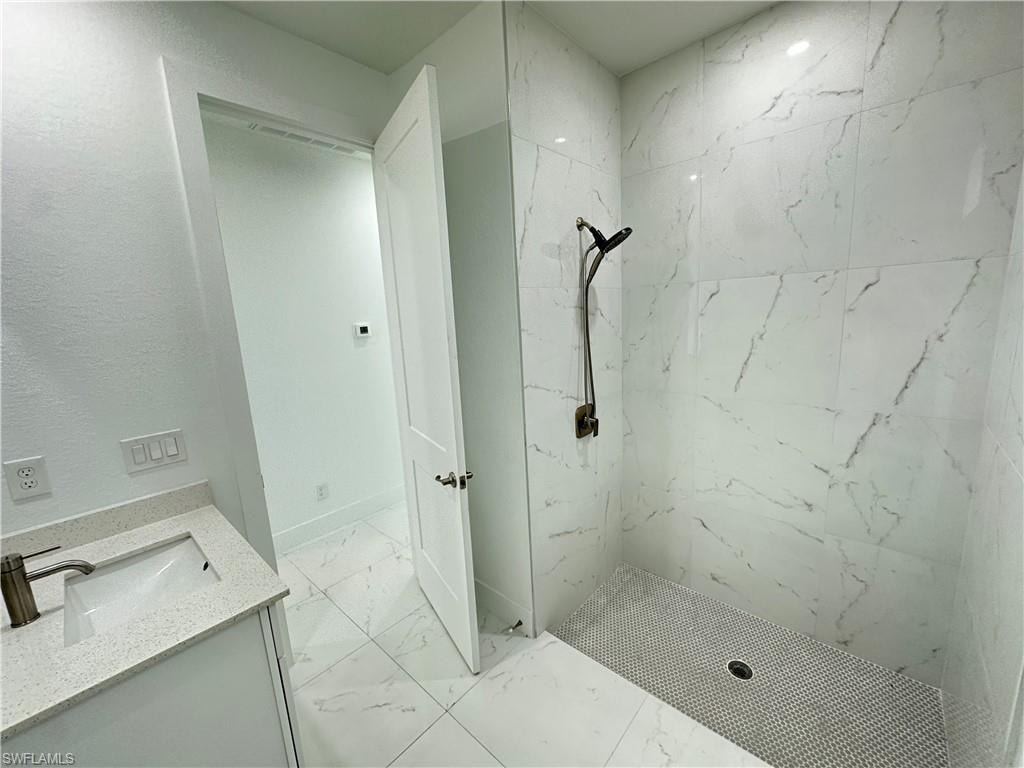 Walk-in shower with large-format marble-look wall tiles and a pebble-style floor