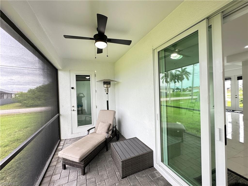 Screened outdoor patio featuring brick paver flooring, a white textured exterior wall, and a black ceiling fan with an integrated light fixture