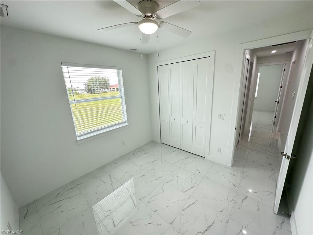 Bright room featuring large format marble-look tile flooring, a ceiling fan with integrated lighting, a window with horizontal blinds, and bi-fold closet doors