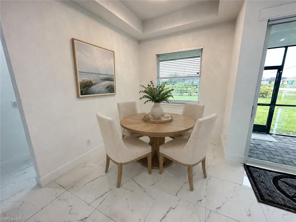 Bright dining area featuring large format white tile flooring with dark veining, a tray ceiling, and a window with horizontal blinds