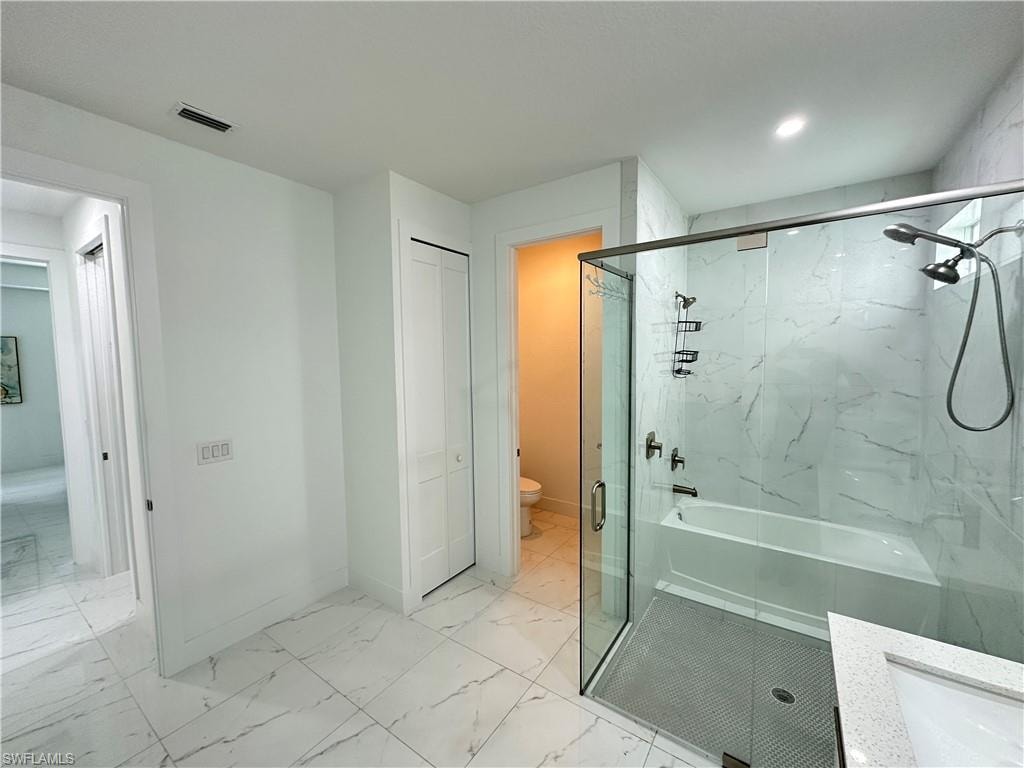 Bathroom featuring a frameless glass shower enclosure, white porcelain bathtub, and white large-format tile flooring
