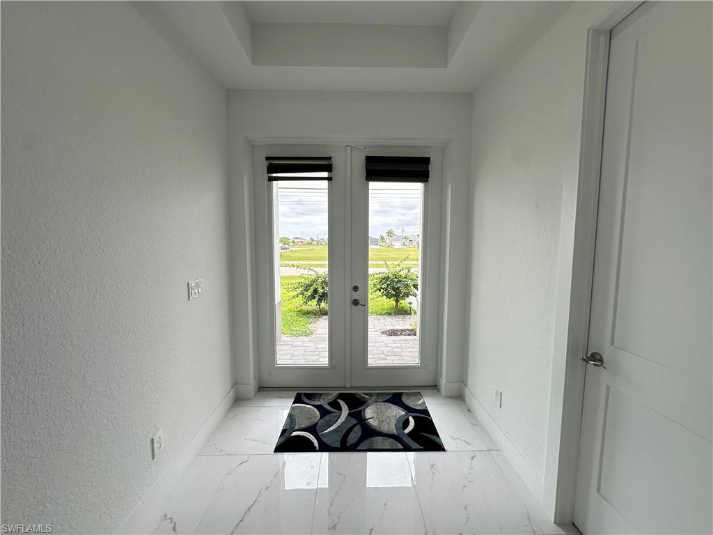 Entryway featuring double French doors, large format tile flooring, a tray ceiling, and white panel doors
