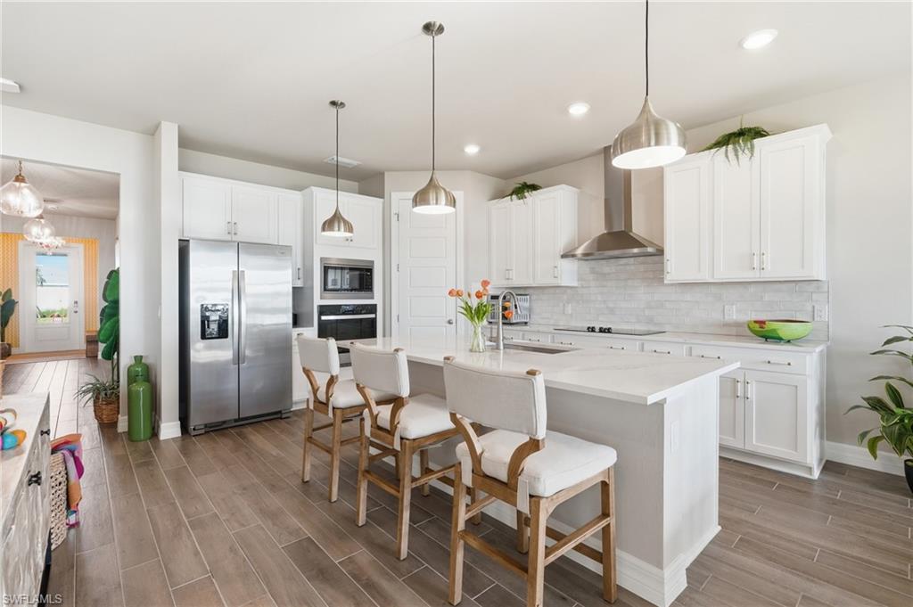Upgraded kitchen with wall oven & stainless steel appliances, a white island with seating, pendant lighting, and wood-finish flooring