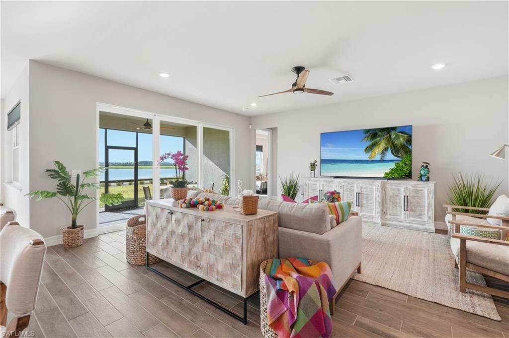 Bright, open-concept living space featuring expansive glass sliding doors with ocean views, wood-finish flooring throughout, a ceiling fan, recessed lighting, and built-in cabinetry