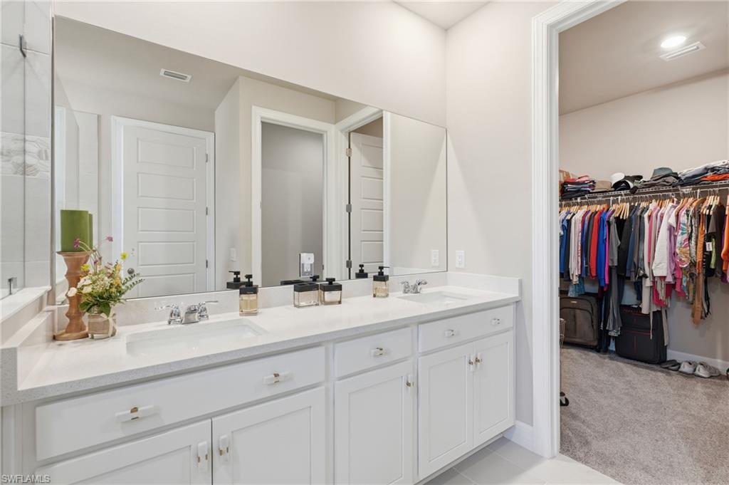 Dual vanity with undermount sinks, white cabinetry, expansive mirror, and a walk-in closet with built-in shelving and carpet flooring