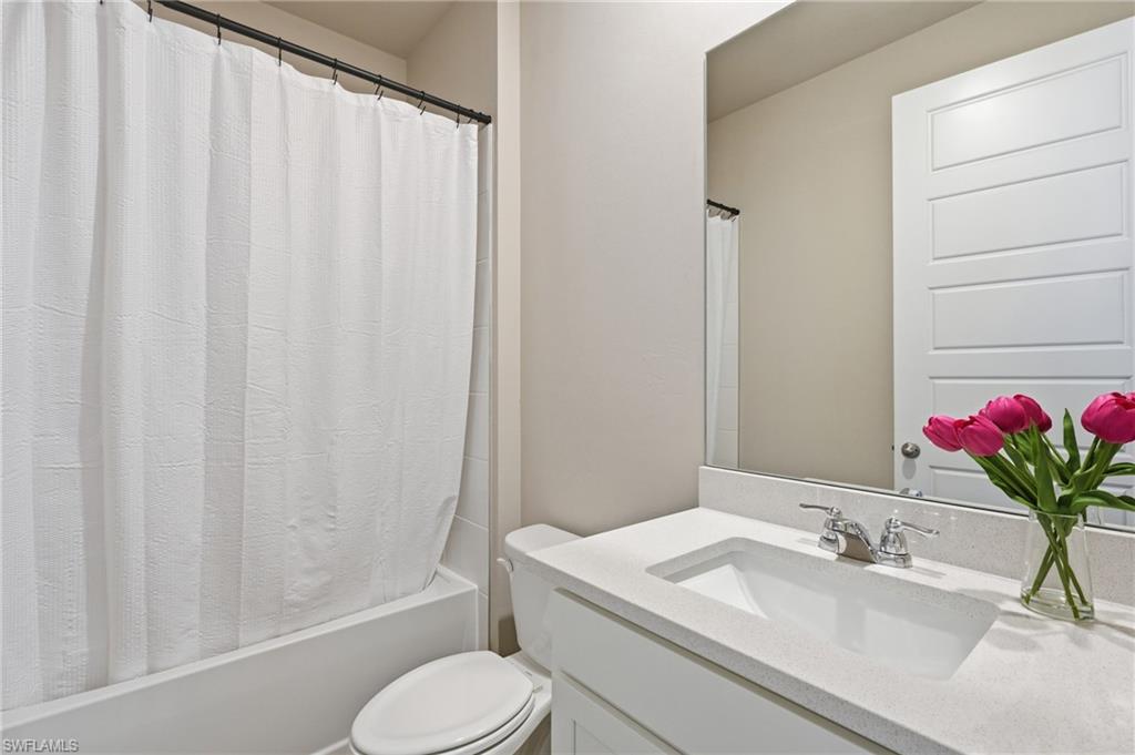 Bathroom featuring a bathtub with shower, toilet, vanity with integrated sink, stone-finish countertop, and wall-mounted mirror
