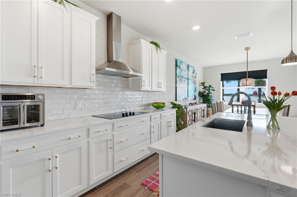 Gourmet kitchen featuring white shaker cabinetry, stainless steel range hood, stone countertops, integrated cooktop, and an undermount sink on the island