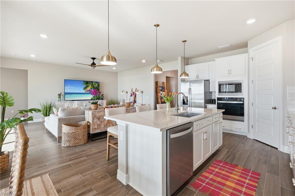 Open-concept living space featuring wood-finish flooring, white kitchen cabinetry, stainless steel appliances, a kitchen island with seating, and recessed lighting