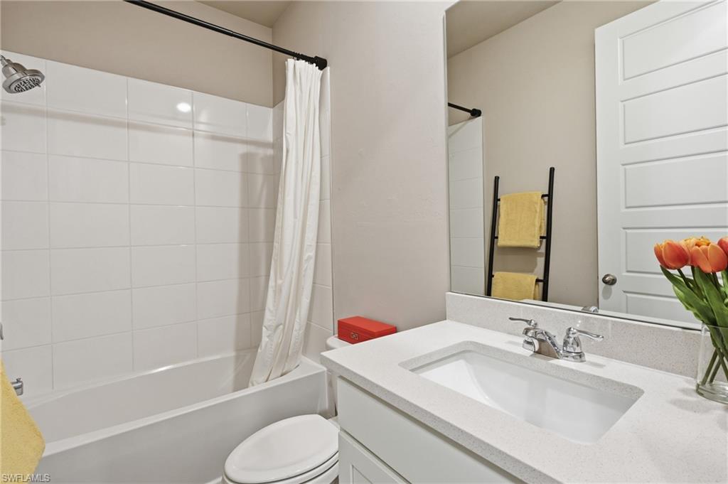 Bathtub with white tile surround, a single vanity with an integrated sink, a chrome faucet, and a large wall-mounted mirror