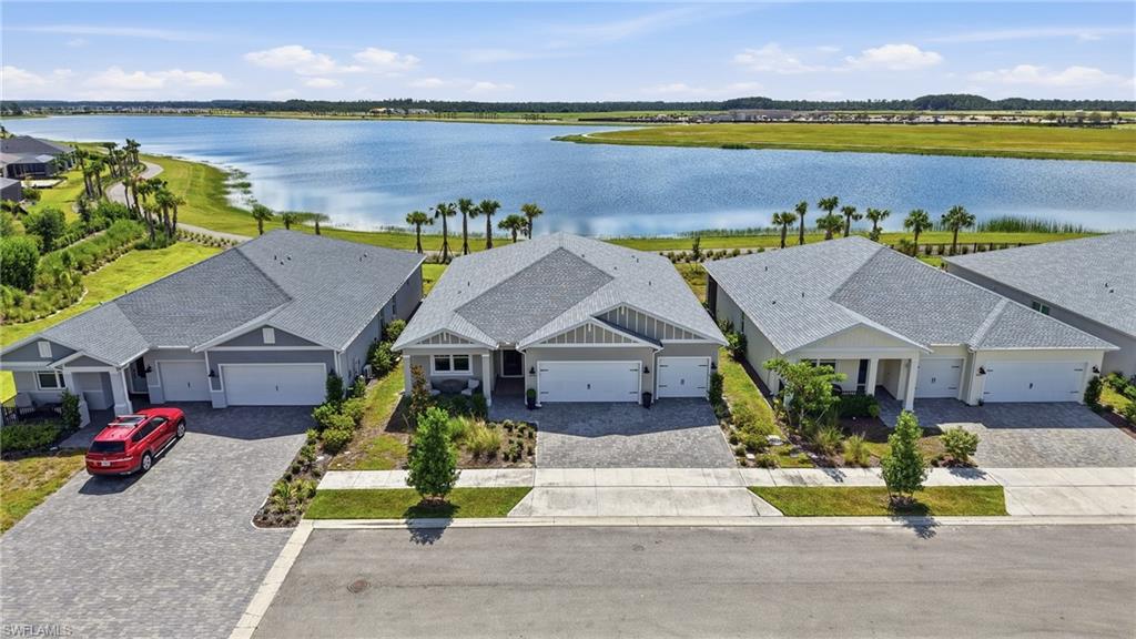 Lakefront property featuring a paver driveway, an attached garage, and mature landscaping