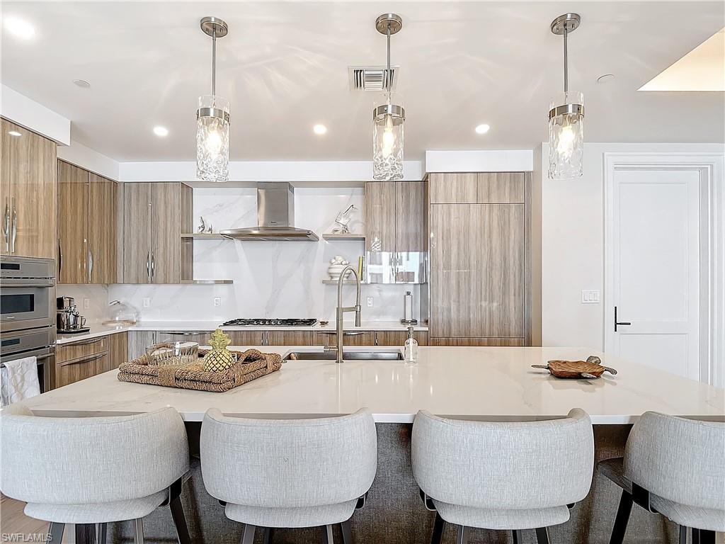 Kitchen with wall chimney range hood, hanging light fixtures, backsplash, and a large island