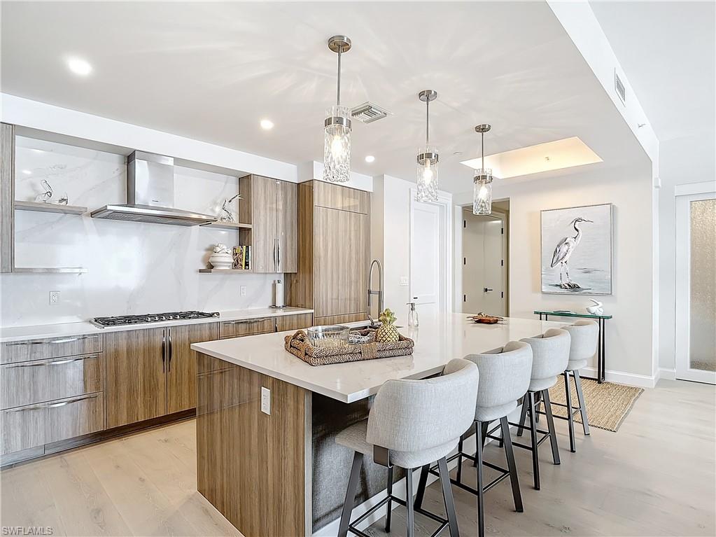 Kitchen with stainless steel gas stovetop, a kitchen island with sink, light hardwood / wood-style flooring, pendant lighting, and ventilation hood