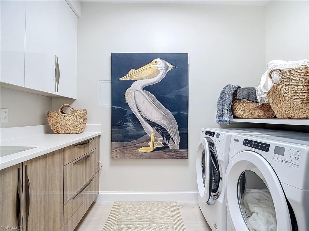 Clothes washing area with cabinets, washing machine and clothes dryer, and light hardwood / wood-style floors