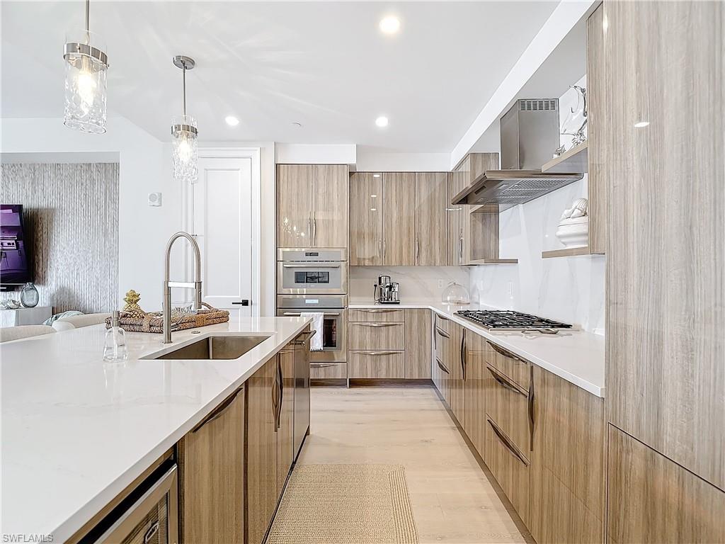 Kitchen featuring wall chimney exhaust hood, hanging light fixtures, stainless steel appliances, sink, and light wood-type flooring