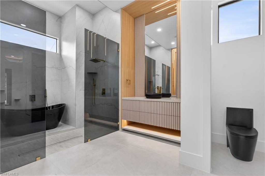 Contemporary bathroom featuring a freestanding black soaking tub, a frameless glass shower enclosure with dark bronze fixtures, and a fluted wood-finish vanity with an integrated sink