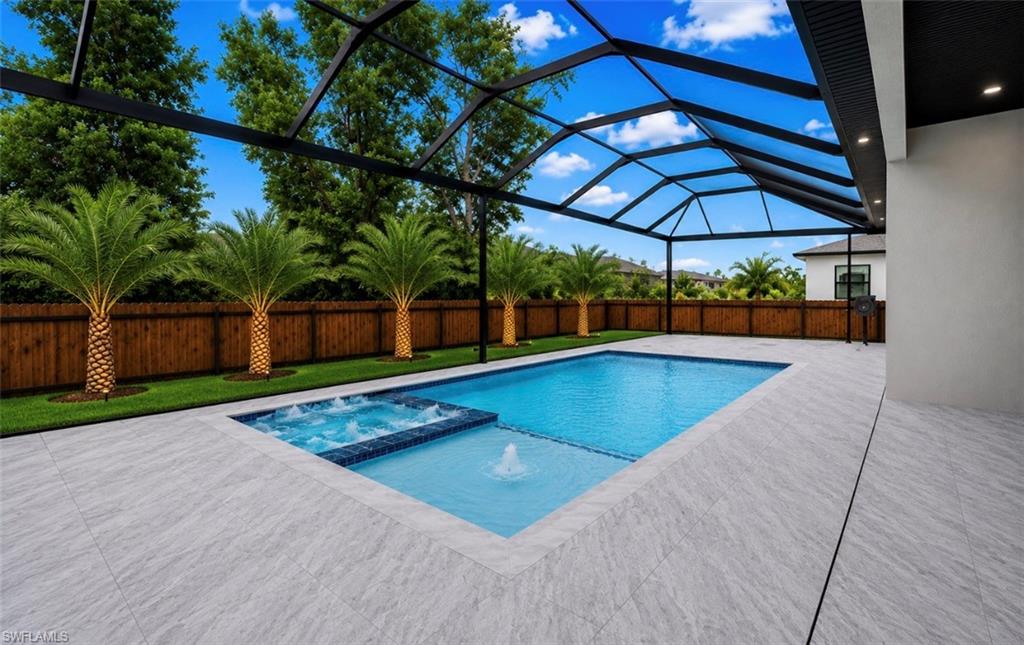 Screened outdoor area featuring a swimming pool with integrated spa and water feature, light-toned patio tile, and a wooden privacy fence with mature palm trees