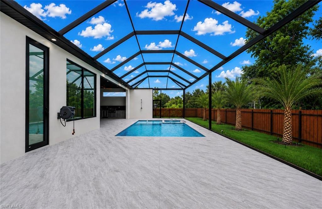 Expansive screened-in pool enclosure featuring a rectangular swimming pool with integrated spa, light gray-toned patio flooring, and a privacy fence bordering lush green landscaping
