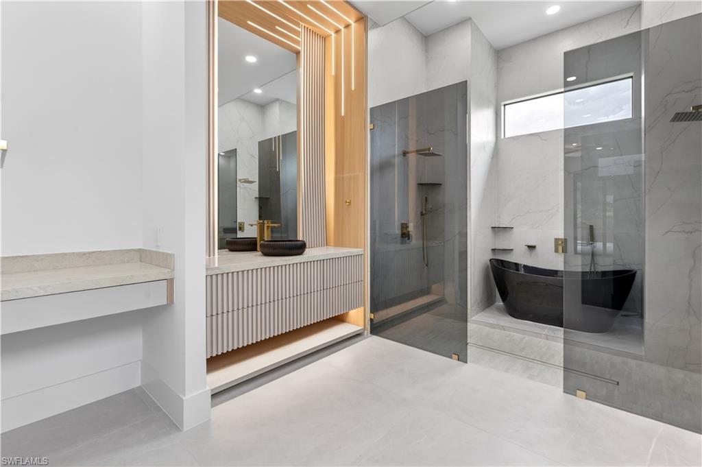 Contemporary bathroom featuring a freestanding black soaking tub, dual glass-enclosed shower areas, and a vanity with reeded cabinetry