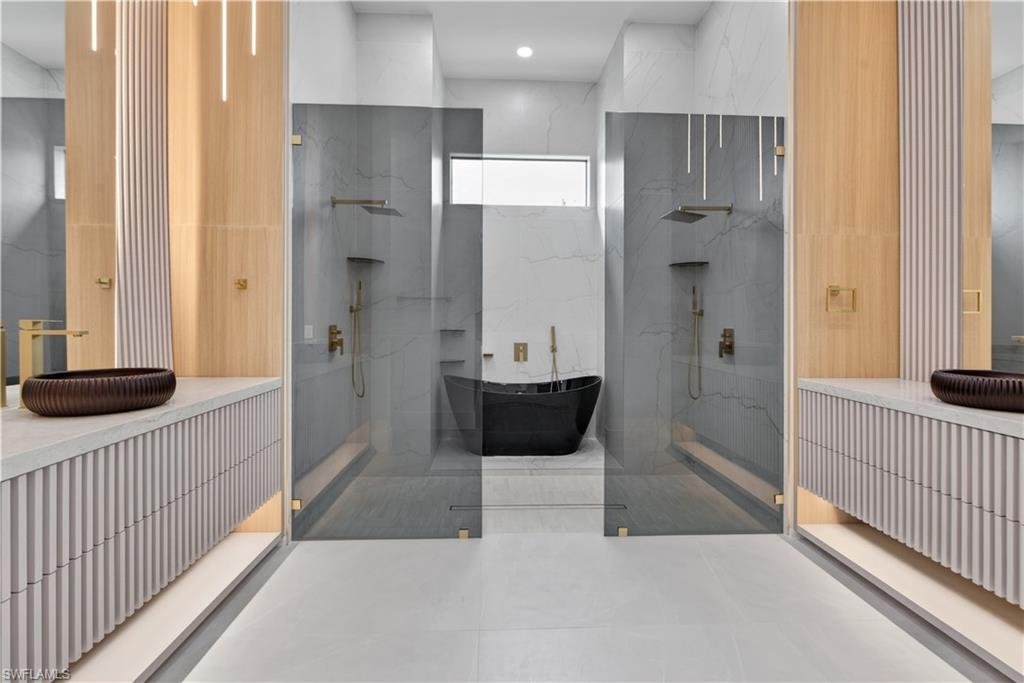 Contemporary bathroom featuring twin walk-in showers with clear glass enclosures and brass fixtures, a freestanding black soaking tub, and dual floating vanities with reeded cabinetry and vessel sinks