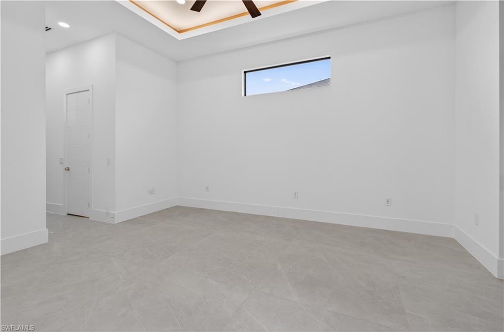 Spacious room featuring light-toned tile flooring, a tray ceiling with recessed lighting, and a modern ceiling fan
