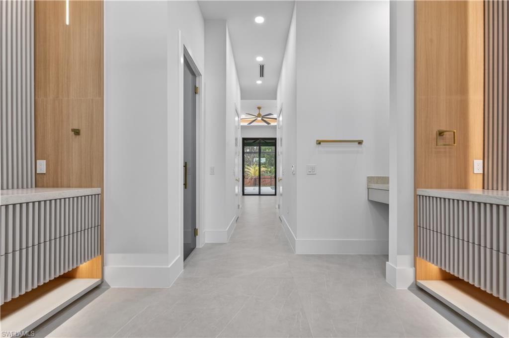 Spacious corridor featuring light wood-finish wall panels, integrated linear lighting, and built-in fluted cabinetry with undermount illumination